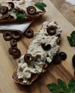 Fermented cashew vegan cream cheese spread with olives on a piece of bread and decorated with fresh black olives.