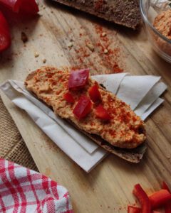 Fermented cashew vegan cream cheese spread with red pepper on a piece of bread and decorated with fresh red peppers.